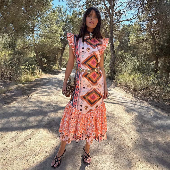 Bridget Print Frida Dress in a multicoloured geometric print with frilled sleeves and a tiered hem on an outdoor path.