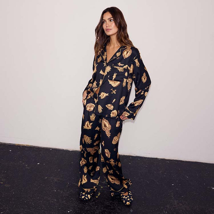 Deloris Button Through Pyjamas in black with gold hand, heart and eye motifs, worn by a model in a full-length studio shot.